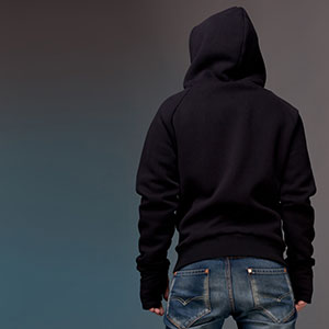A man in jeans and a hoodie standing on a gray background.